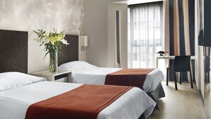 A hotel room with two beds, a desk, a chair, and a vase with flowers. - Two Hotel Buenos Aires (Buenos Aires)