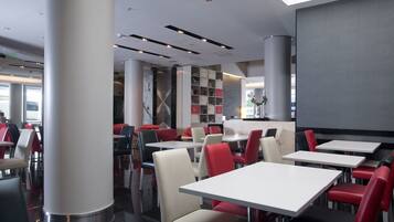 Un interno ristorante moderno con soffitti alti, illuminazione a scomparsa e un mix di sedute rosse e bianche.