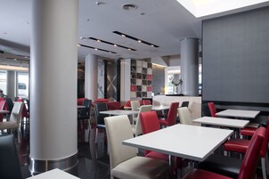 Ein modernes Restaurant-Interieur mit hohen Decken, eingelassener Beleuchtung und einer Mischung aus roten und weißen Sitzgelegenheiten.