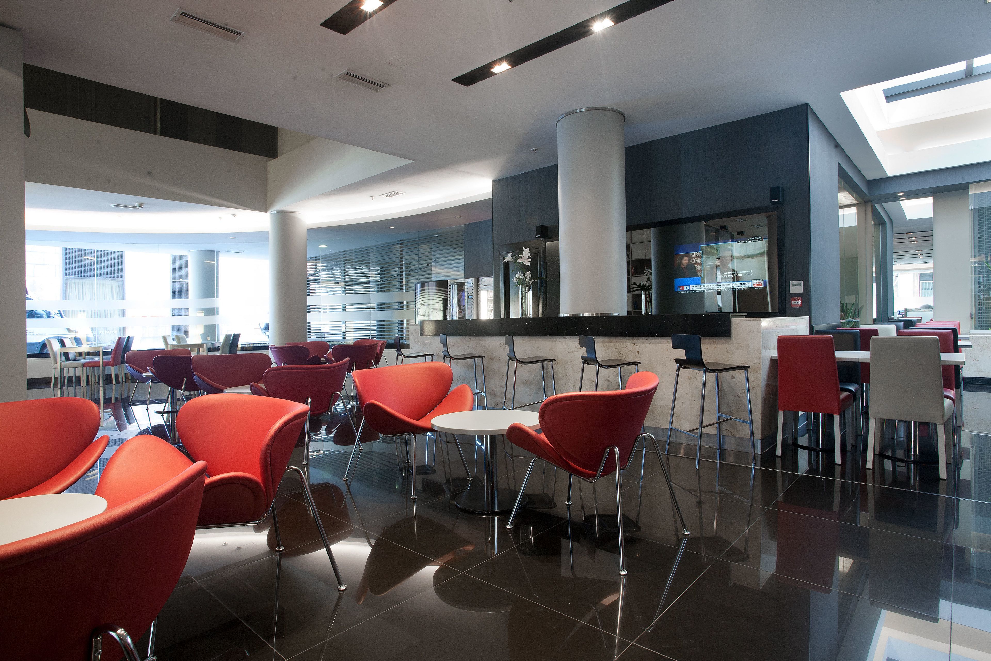 A modern dining area with red chairs and a white table, featuring a glass partition and a bar area in the background.