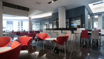 A modern dining area with red chairs and a white table, featuring a glass partition and a bar area in the background.