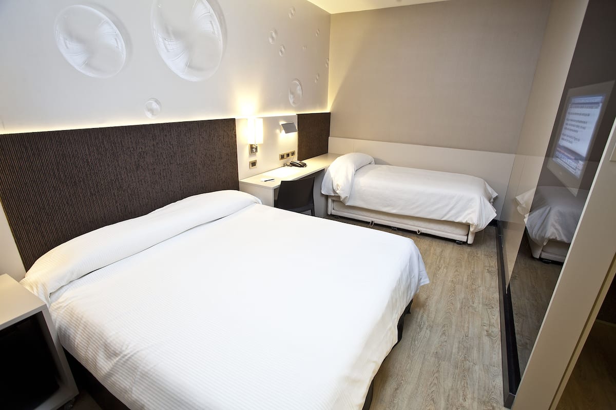 A hotel room with two beds, a desk, a chair, and a mirror.