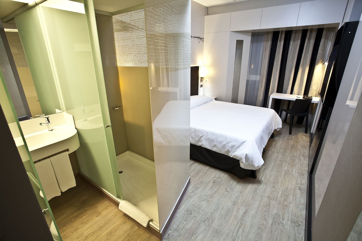 A compact hotel room with a bed, a desk, and a shower area.