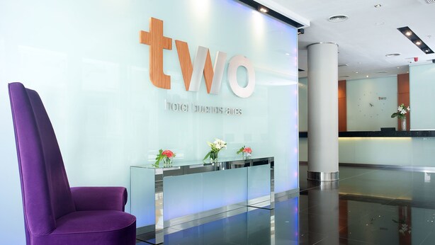 A reception area with a purple chair, a glass desk with flowers, and a wall displaying the hotel name 'tWO'. - Two Hotel Buenos Aires (Buenos Aires)