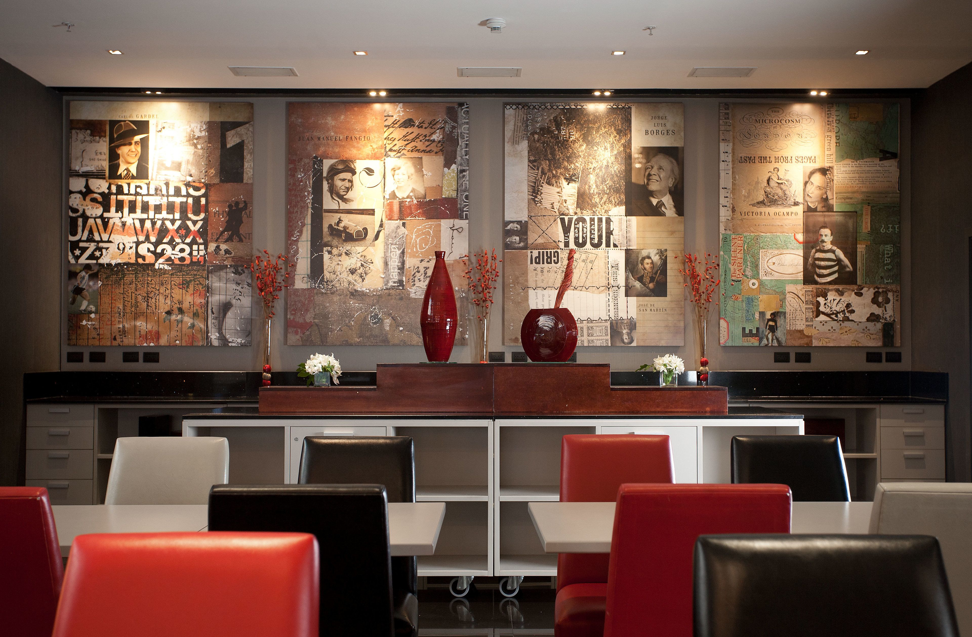 Un restaurante con una decoración moderna, que presenta una larga barra con sillas rojas y blancas, y una pared decorada con diversos carteles y fotografías.