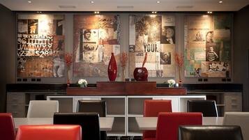 A restaurant with a modern interior, featuring a long counter with red and white chairs, and a wall adorned with various posters and photographs.