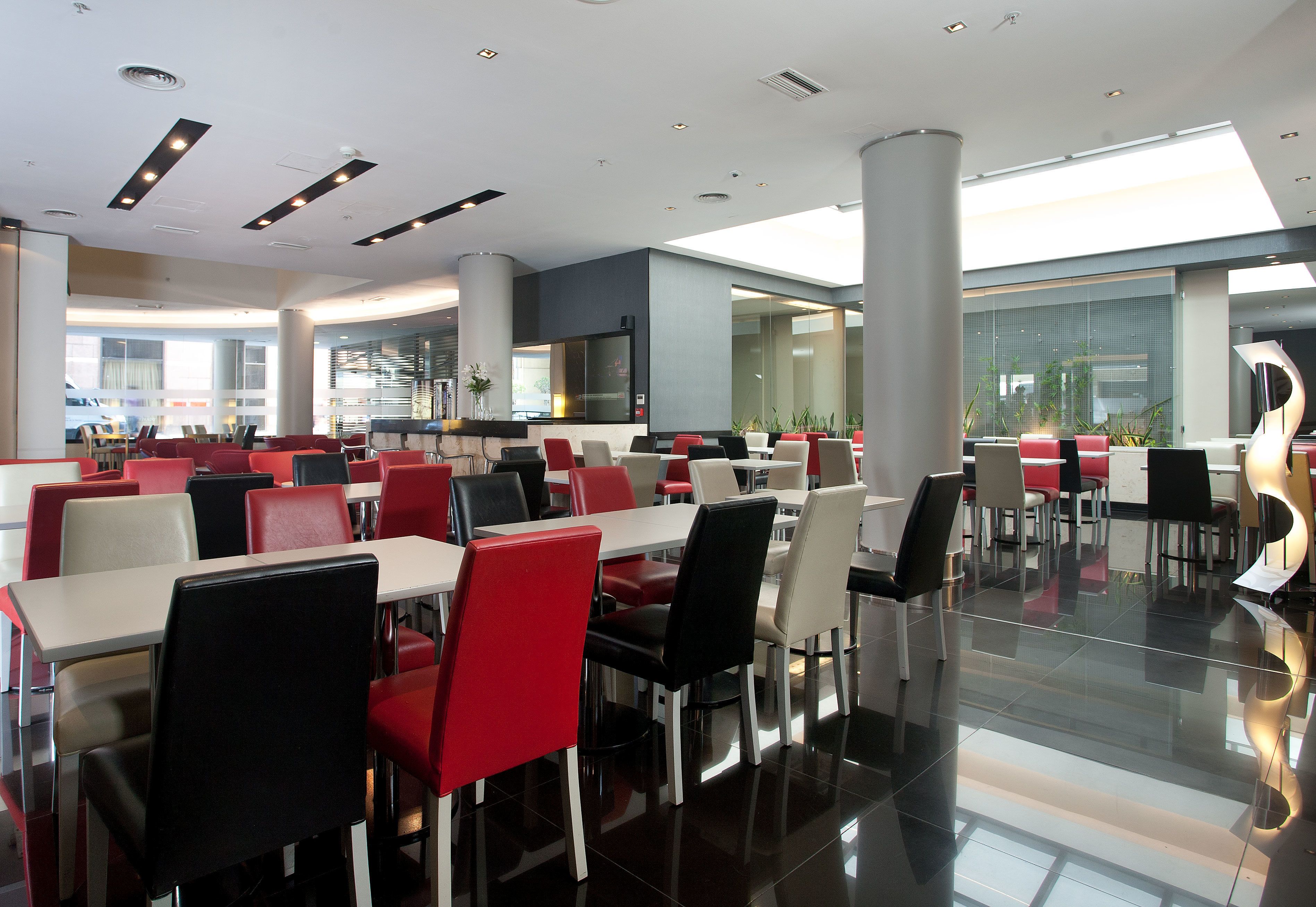 A modern dining area with multiple tables and chairs, large windows, and a clean, polished floor.