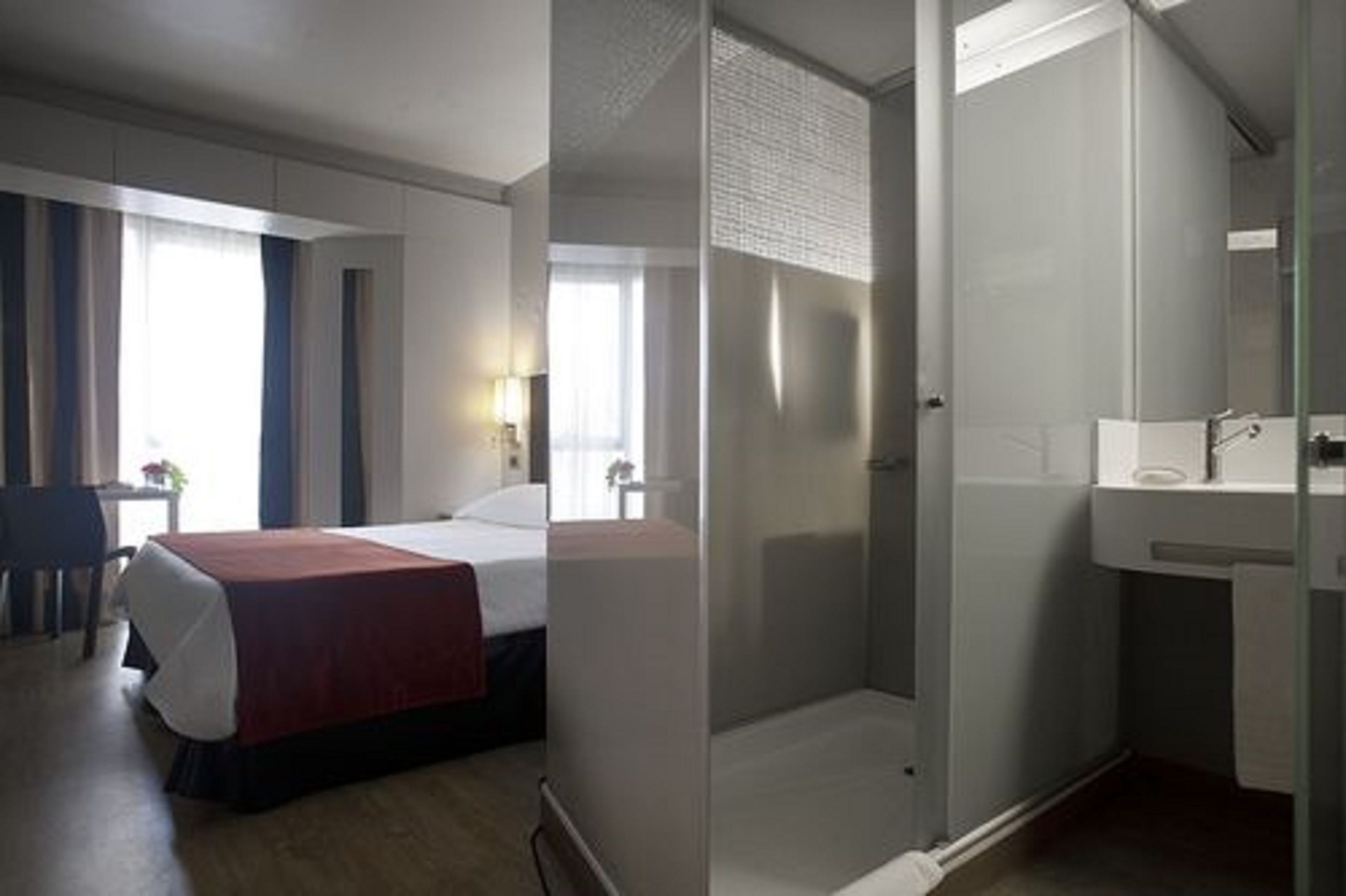 A hotel room with a bed, a desk, a chair, a shower, and a sink.