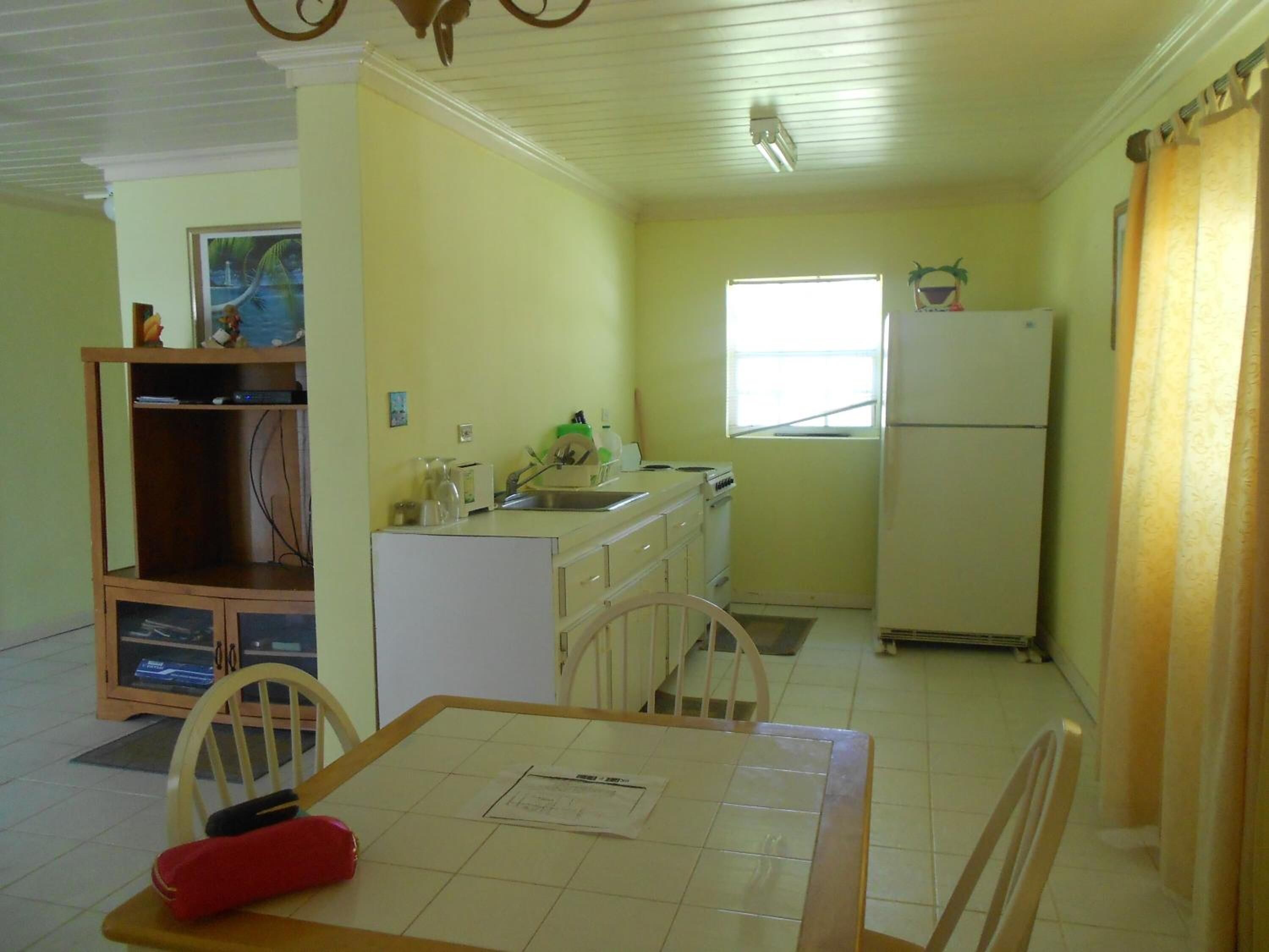 A compact kitchen with white cabinets, a refrigerator, and a window.