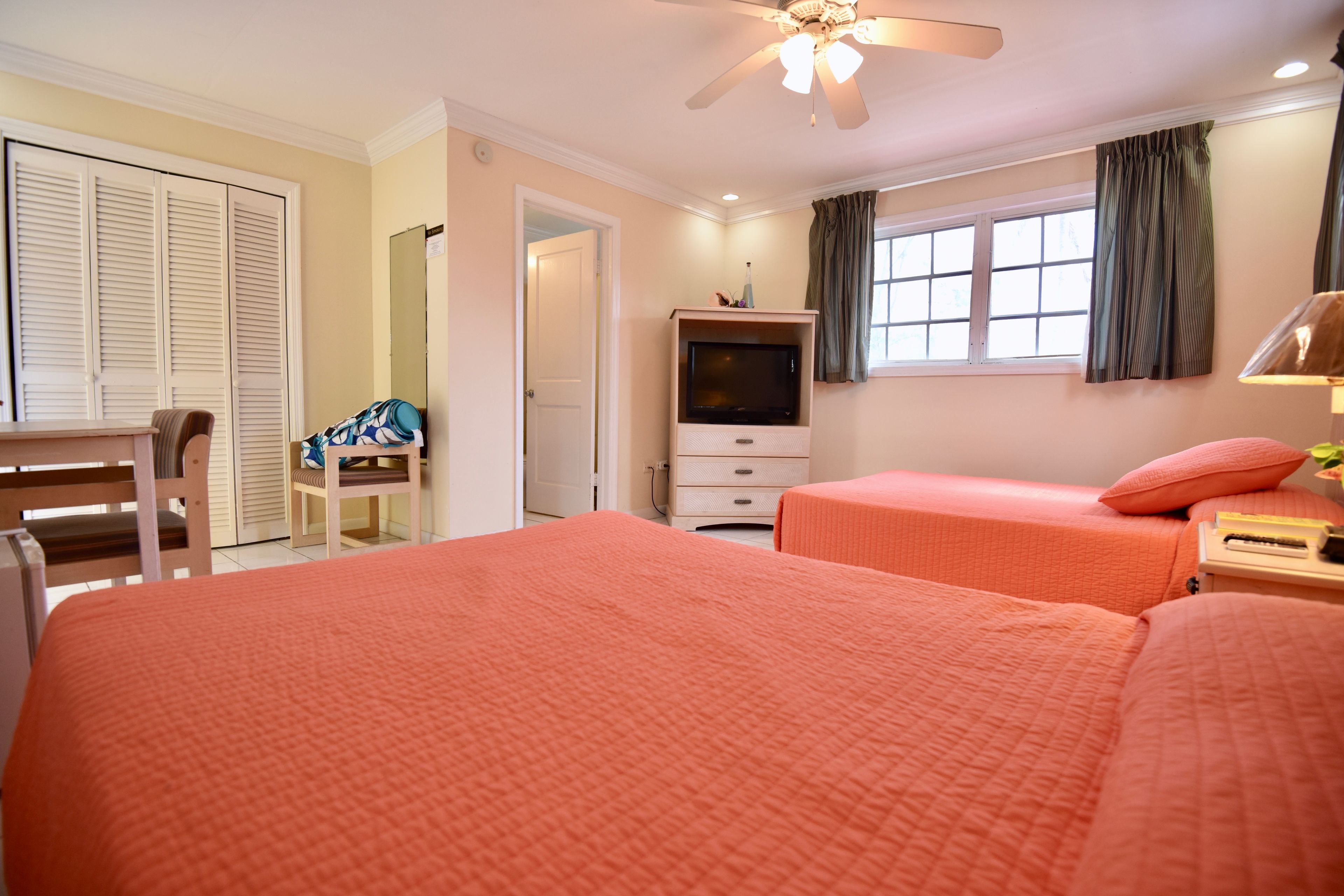 A hotel room with two beds, a desk, a chair, a TV, and a window with curtains.