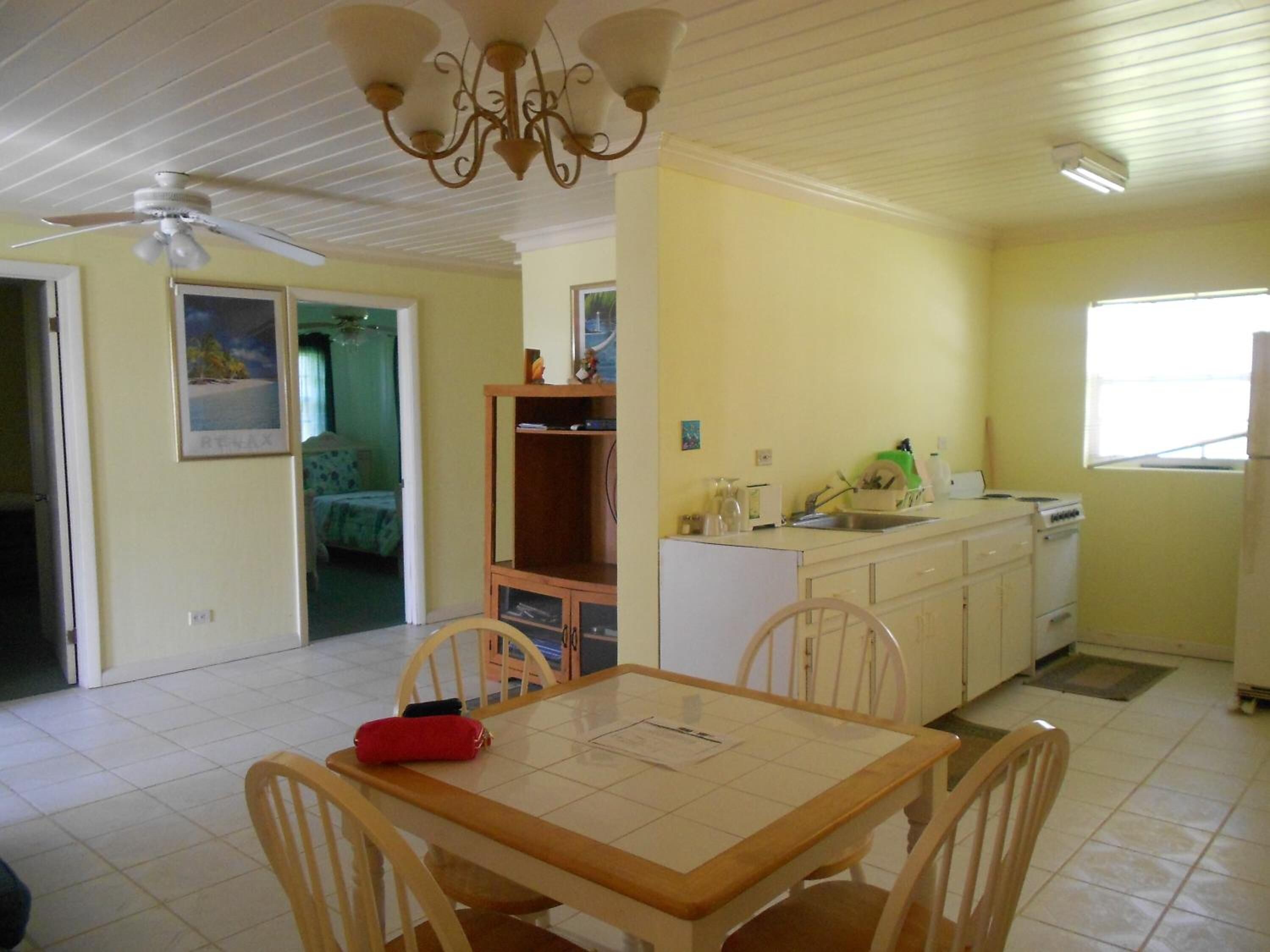 Une cuisine de taille réduite avec des meubles blancs, une table à manger et quatre chaises, un ventilateur de plafond et une fenêtre qui laisse entrer la lumière naturelle.