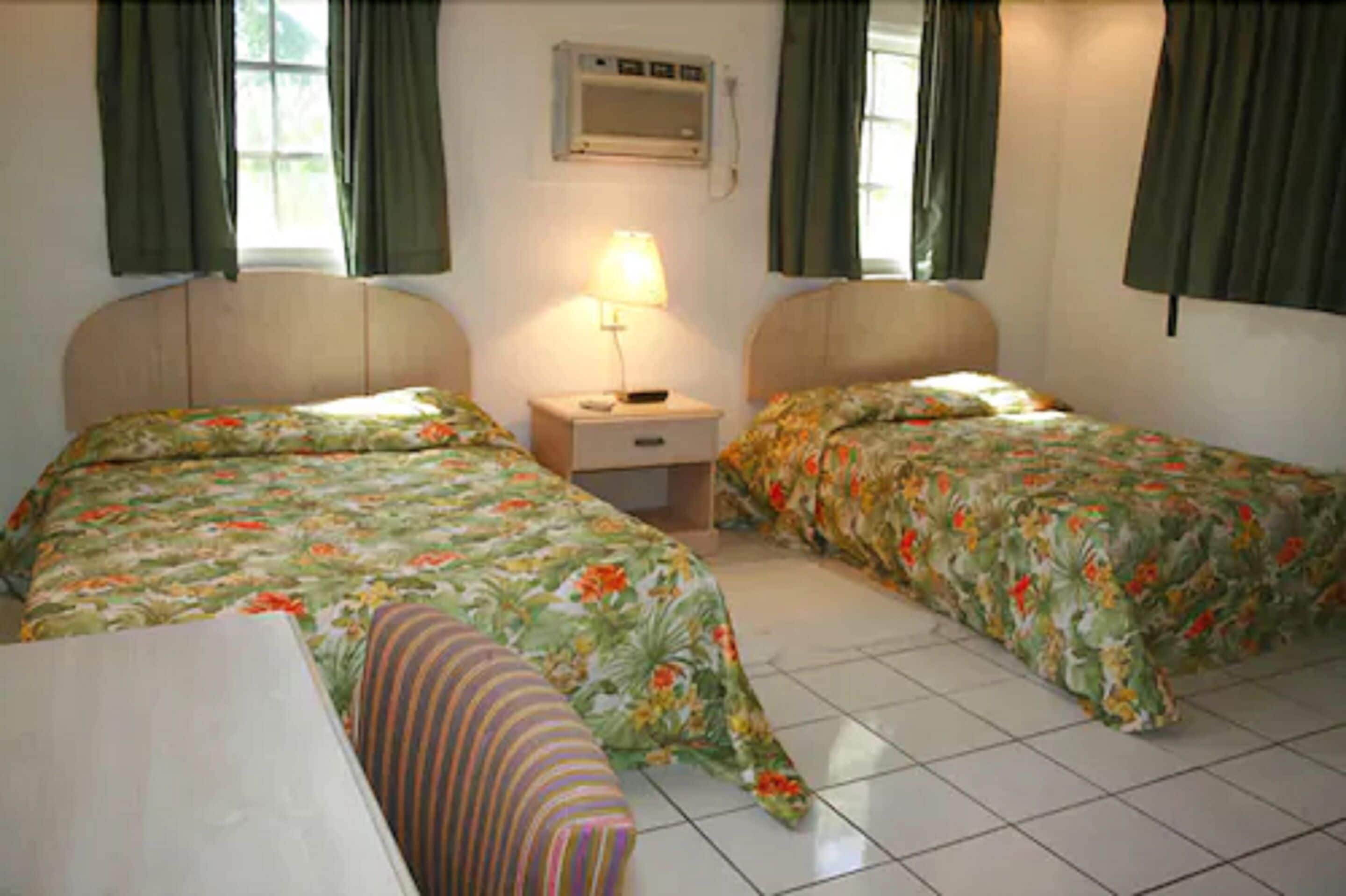 A room with two beds, a small table, and a nightstand with a lamp.