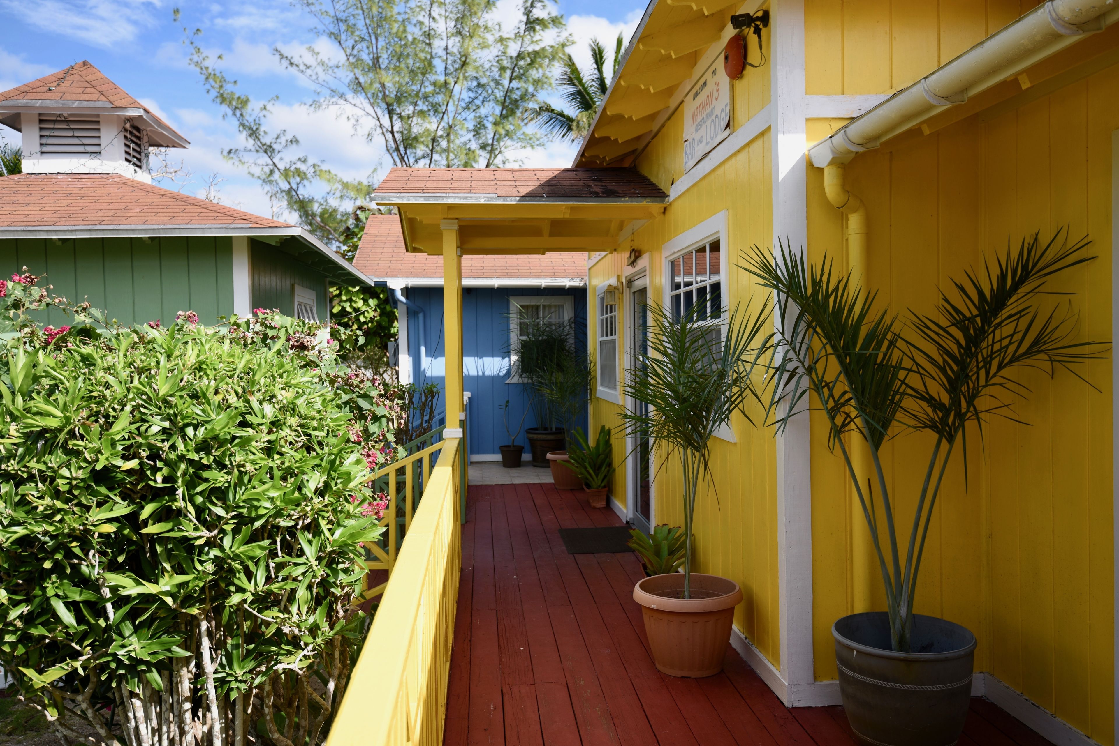 Un bâtiment jaune avec un toit rouge, une véranda et des plantes en pot.
