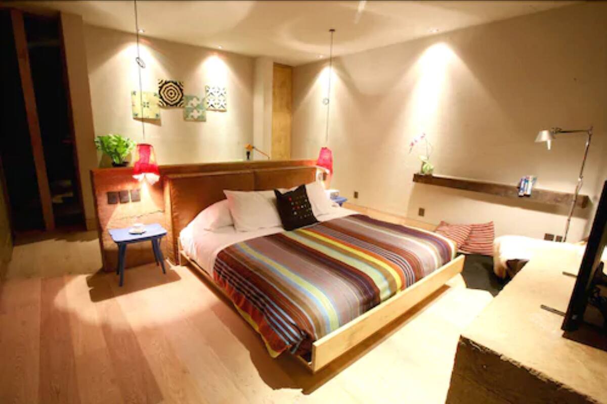 Une chambre à coucher avec un lit en bois, des tables de chevet, un bureau et une étagère ornée d’objets décoratifs.
