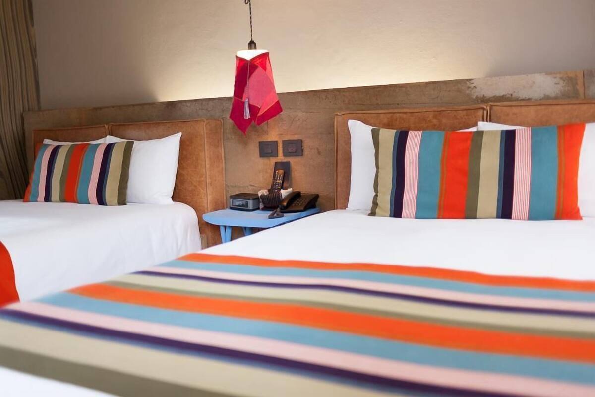 Une chambre d’hôtel avec deux lits, une table de chevet, un téléphone et une lampe suspendue rouge.