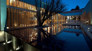 Een modern gebouw met grote ramen, een reflecterend zwembad en terrasplekken.