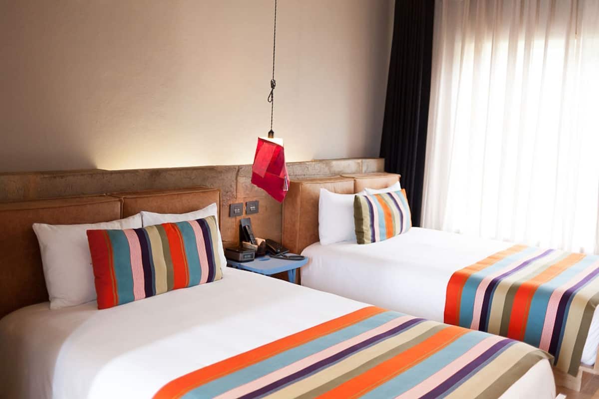 Une chambre d’hôtel avec deux lits, une table de chevet, un téléphone et un luminaire suspendu.