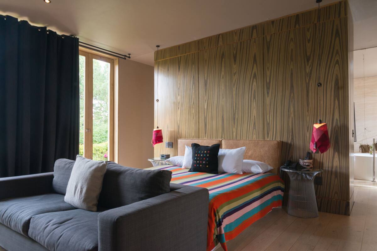 Une chambre à coucher moderne avec un grand lit, un canapé gris, un mur d’accent en bois et une petite table d’appoint.