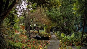A pathway flanked by lush greenery and red flowers, leading through a garden area.