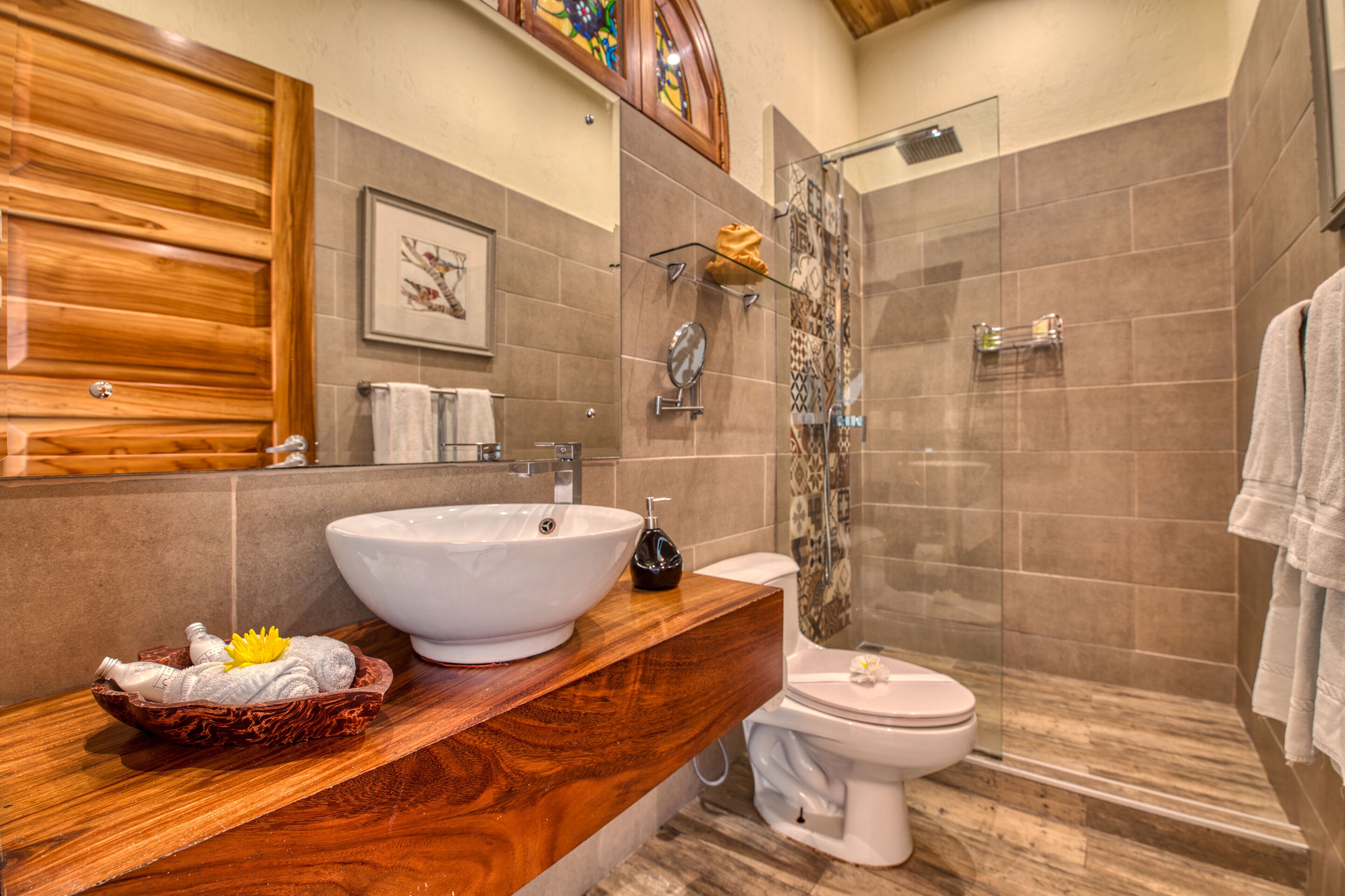 A bathroom with a wooden vanity, a white sink, a toilet, and a glass shower enclosure.