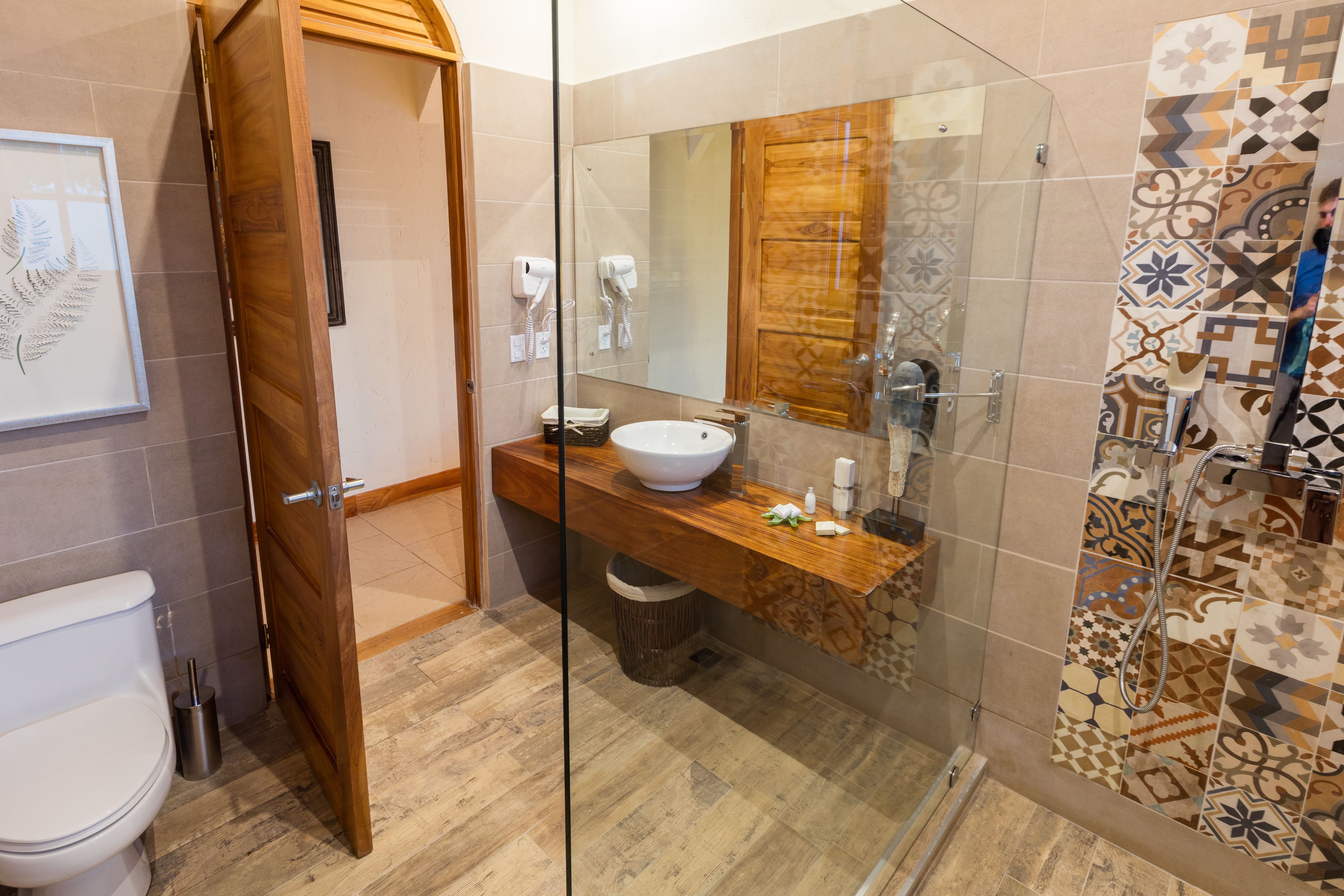 Ein Badezimmer mit einem Holzkosmetikschrank, einem weißen Waschbecken, einer Glasdusche und einem Spiegel.