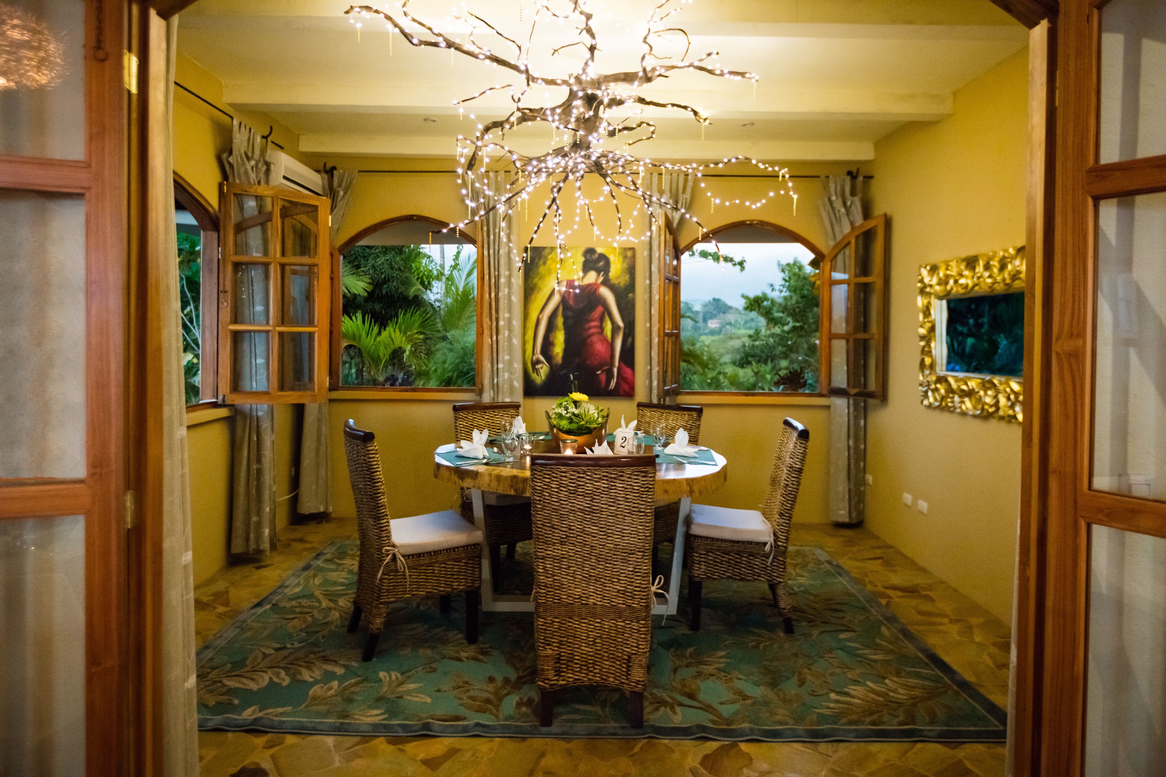 A dining area with a round table, wicker chairs, and a chandelier.