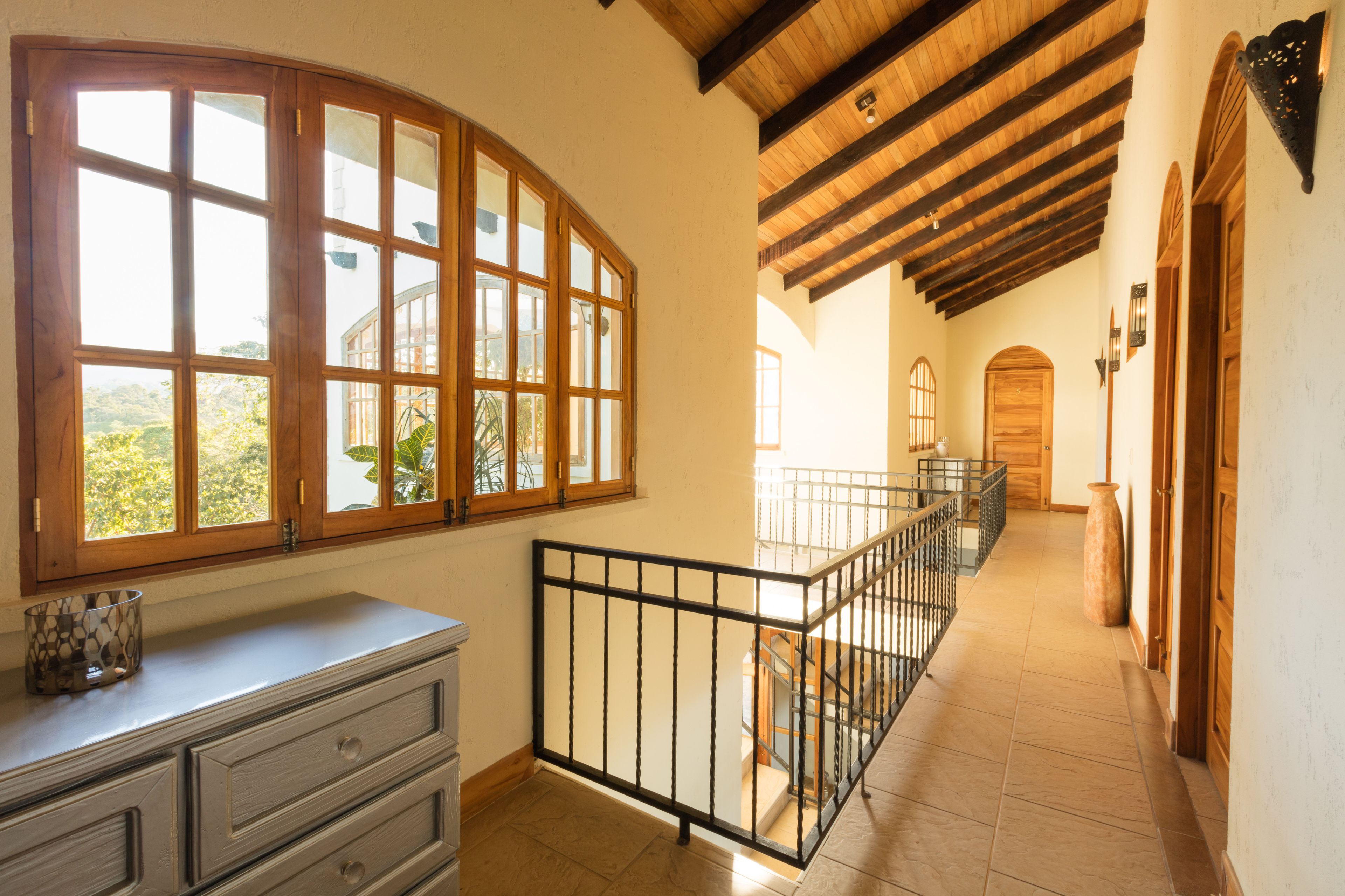 A spacious hallway with wooden beams, a staircase, and a large window with multiple panes.