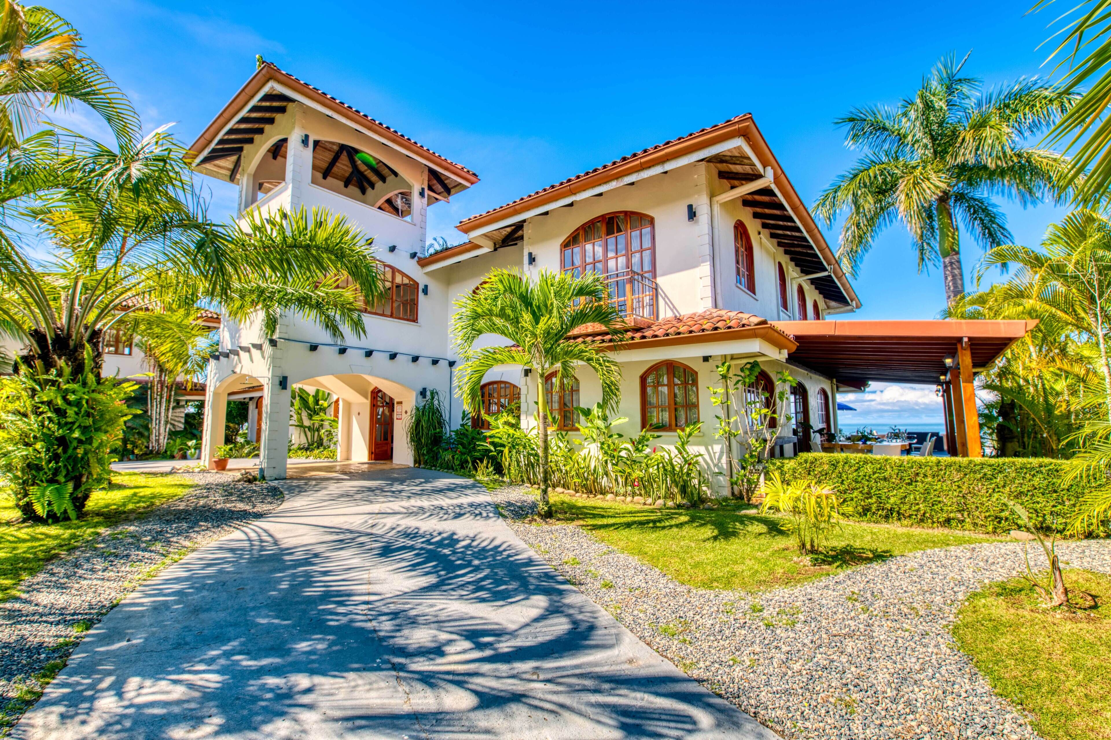 A two-story house with a paved driveway, surrounded by palm trees and a well-maintained lawn.