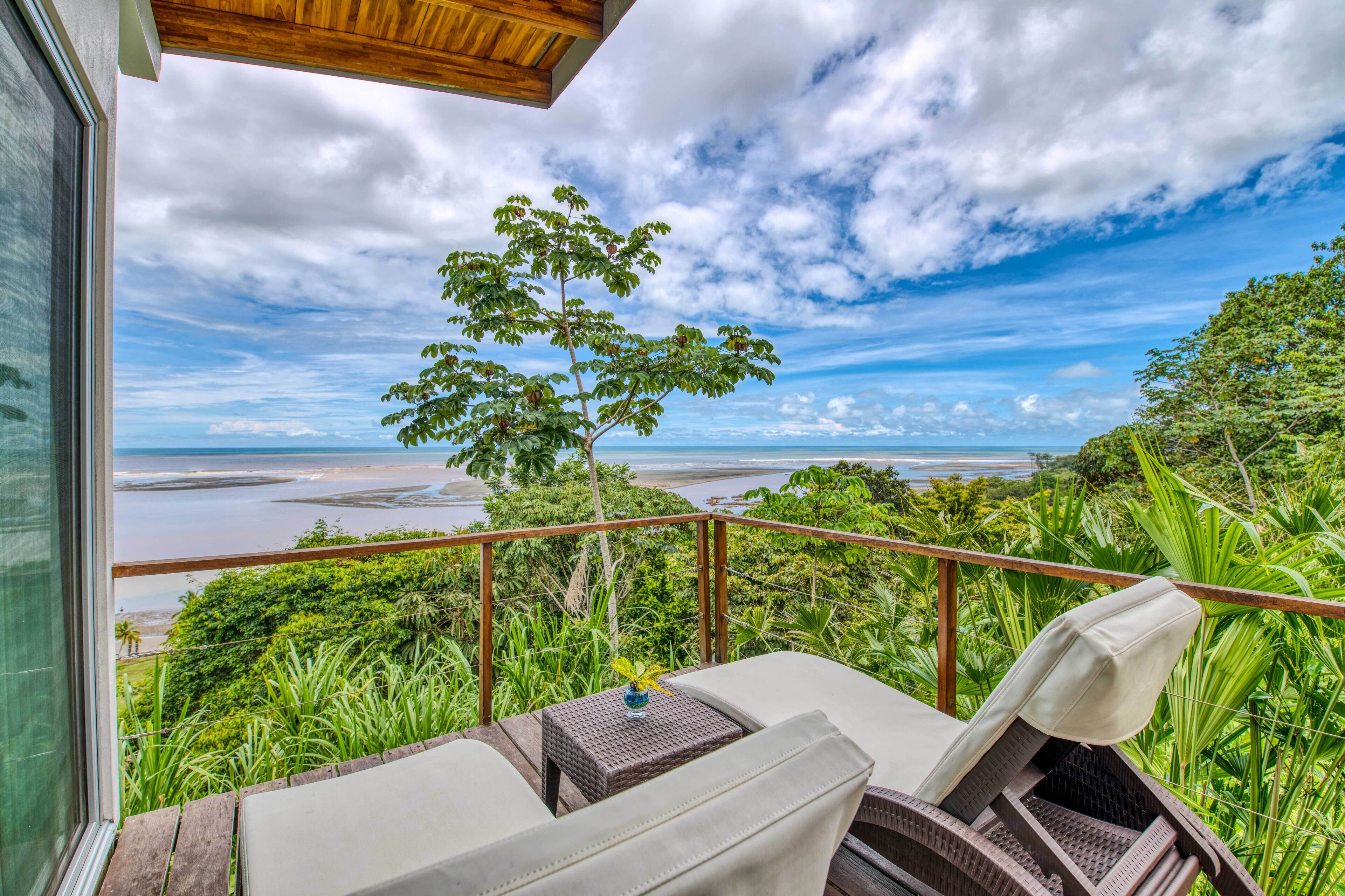 Ein Balkon mit Blick auf Strand und Meer, ausgestattet mit zwei Liegestühlen und einem kleinen Tisch.