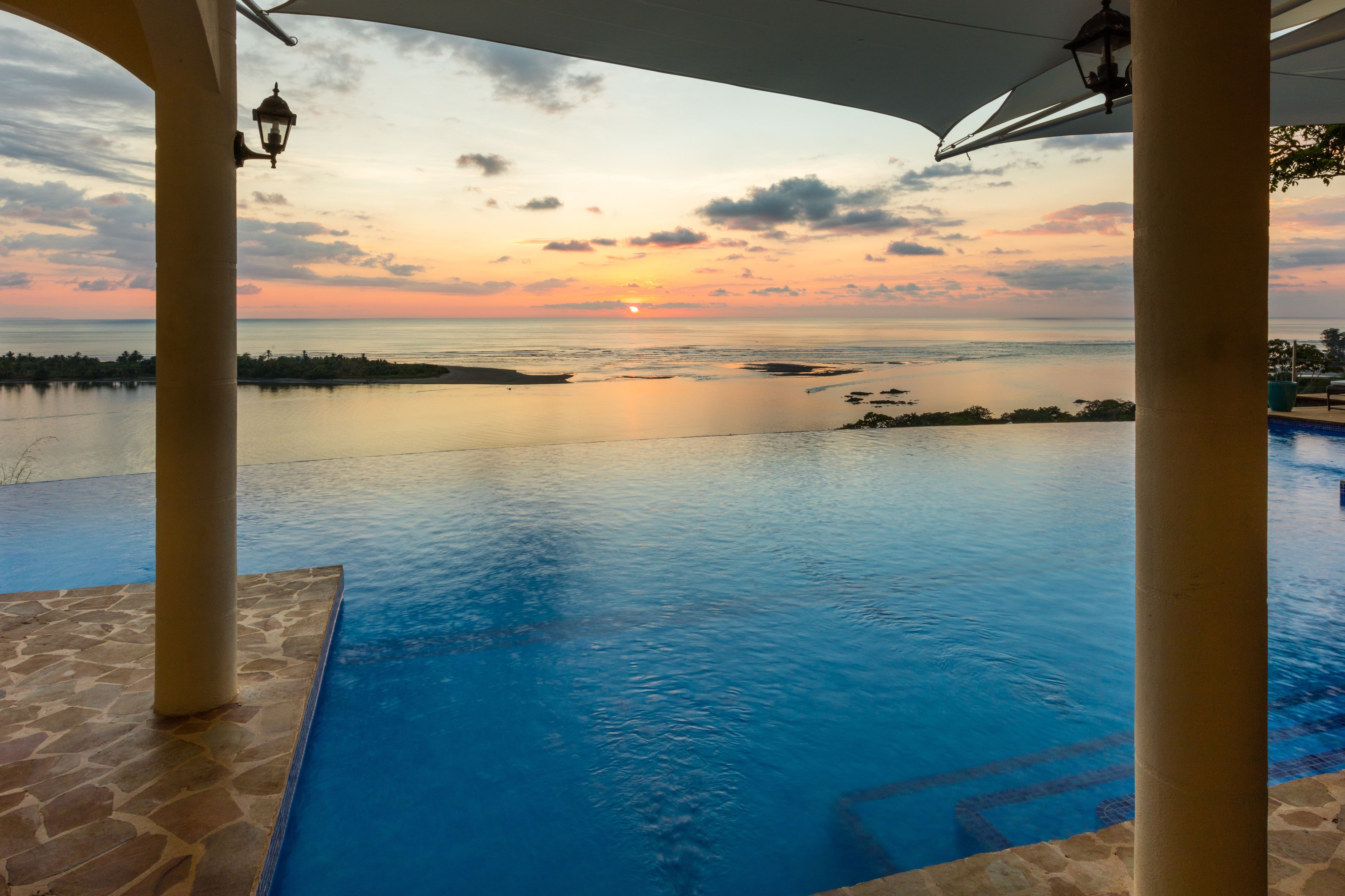 Una piscina infinita con vistas al atardecer, suelo de piedra y columnas.