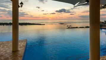 Una piscina infinita con vistas al atardecer, suelo de piedra y columnas.