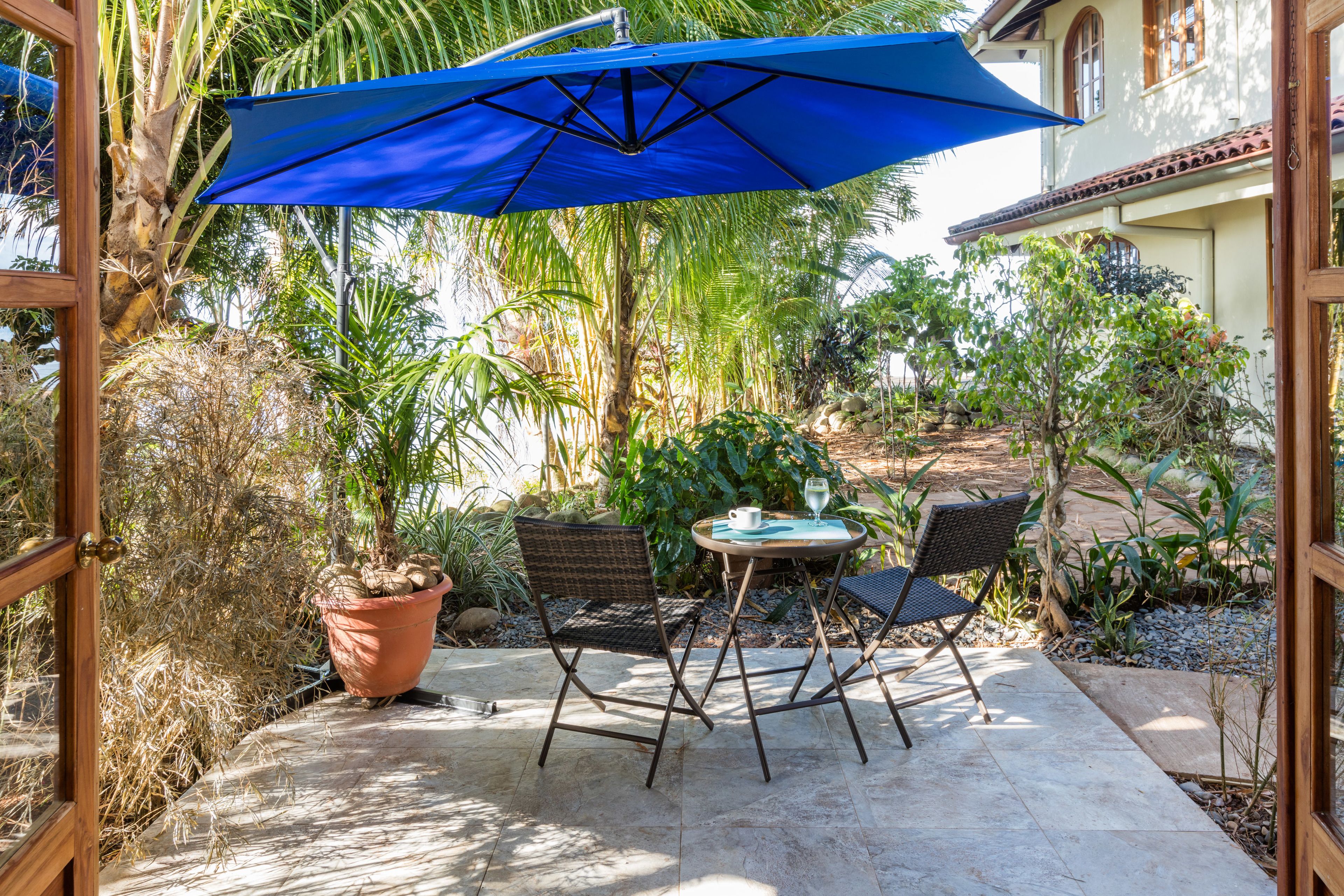 Eine Terrasse im Freien mit Tisch, Stühlen, einem blauen Sonnenschirm und Kübelpflanzen.