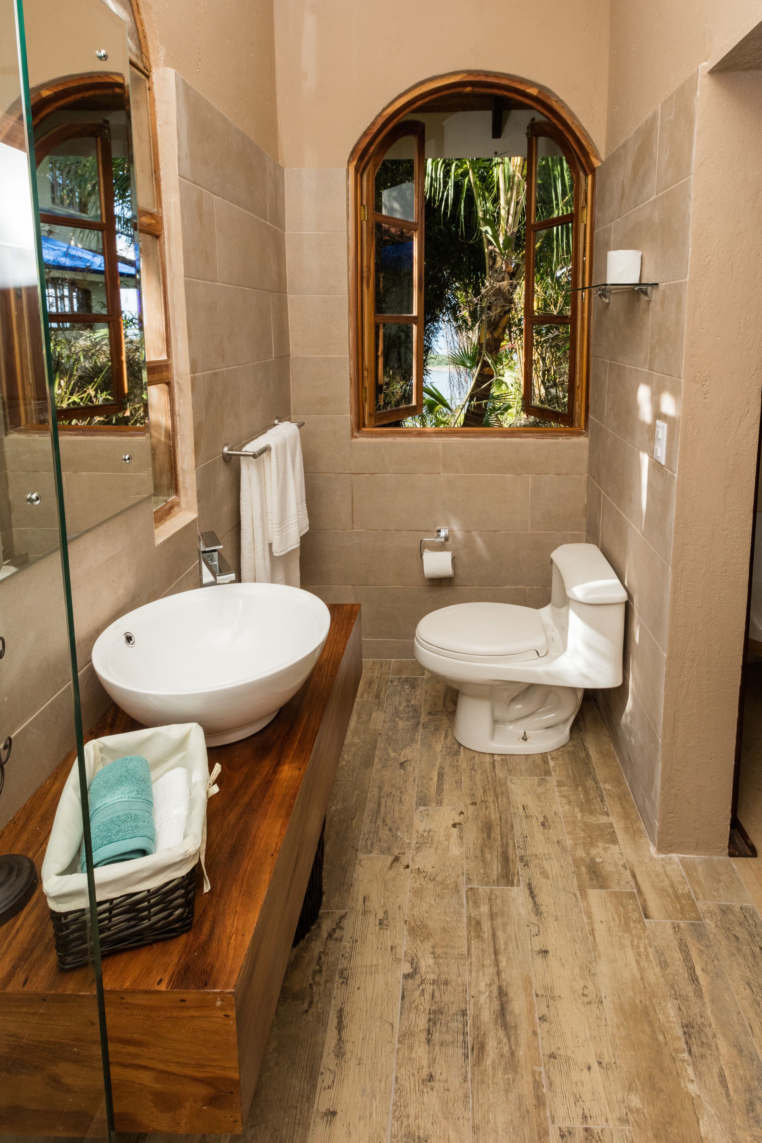 Une salle de bain avec un grand lavabo ovale, des toilettes, un miroir et une fenêtre donnant sur un paysage verdoyant.