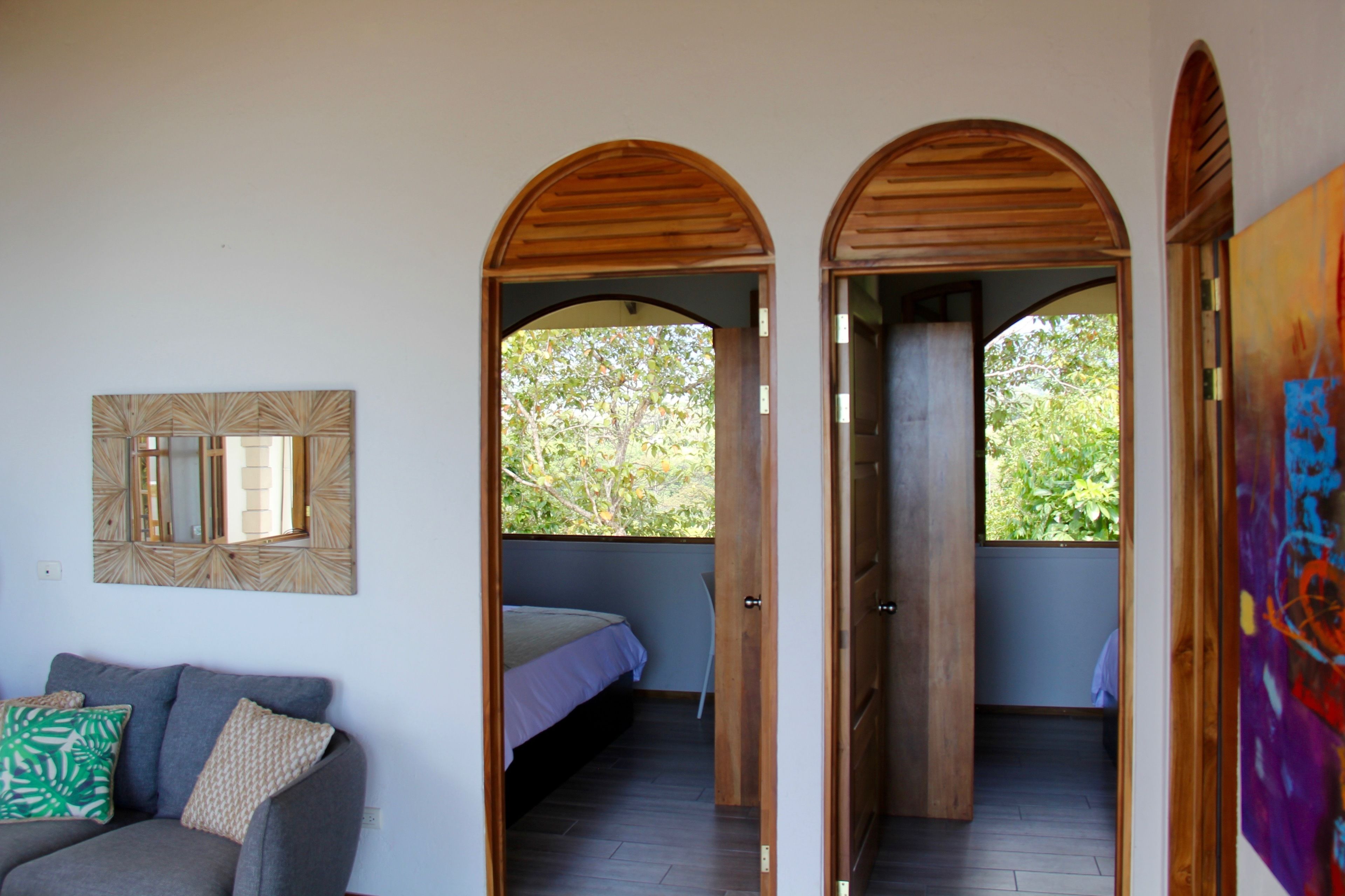 Une pièce comprenant un lit, un canapé et un tableau. On y trouve des portes en bois et une fenêtre donnant sur des arbres.