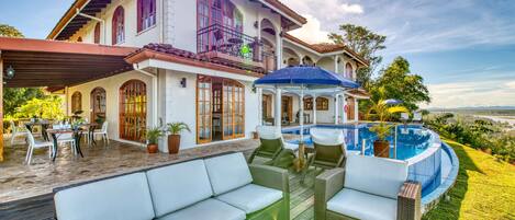 Una casa grande con piscina, mobiliario exterior y un patio cubierto.