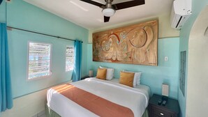 Une chambre à coucher comprenant un lit, un ventilateur de plafond, un climatiseur fixé au mur et une fenêtre avec des rideaux.