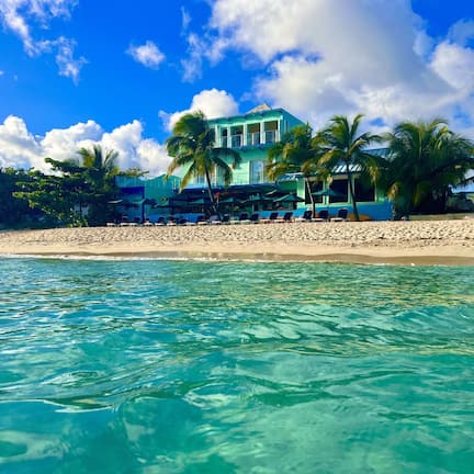 A beachfront hotel with a pool, palm trees, and a clear blue sky.