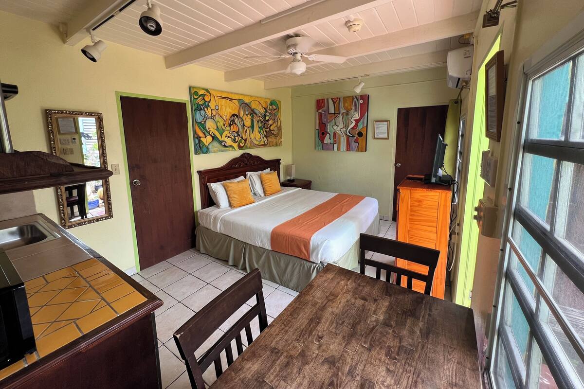 A hotel room with a bed, a desk, a chair, a window, and artwork on the walls.