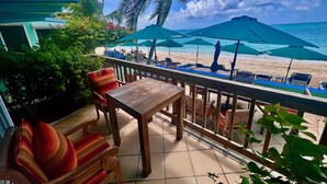 Une terrasse avec des meubles en bois, une vue sur la plage et des parasols verts.