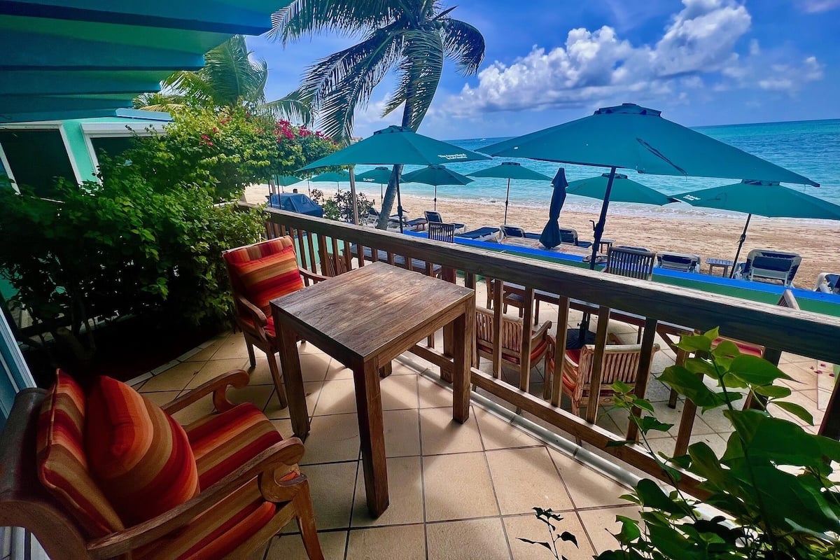 A terrace with wooden furniture, a view of the beach, and green umbrellas.