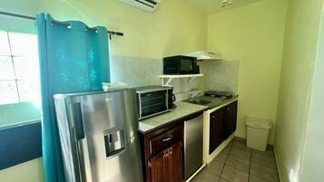 Una cocina compacta equipada con refrigerador, microondas, tostadora, pileta y alacenas.