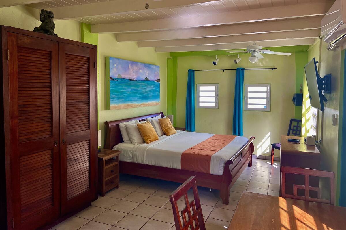A bedroom with a bed, wooden furniture, a painting, and a ceiling fan.