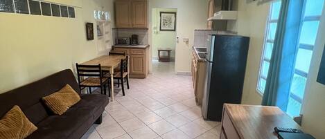 A compact kitchen with a dining area, a sofa, and a refrigerator.
