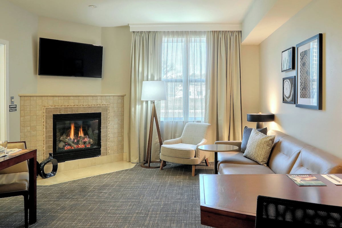 A living room with a fireplace, a sofa, a chair, a coffee table, and a flat-screen TV mounted on the wall.