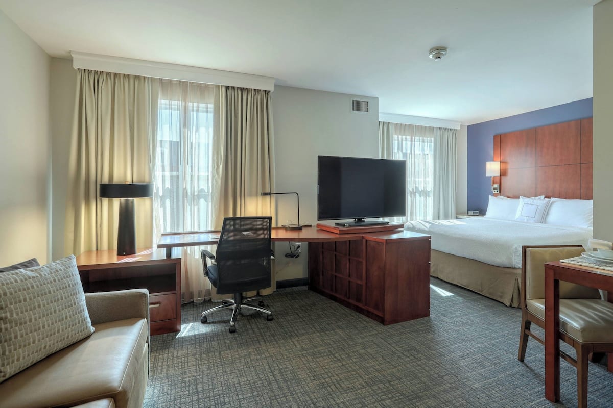 A hotel room with a bed, a desk with a computer, a TV, a chair, and a sofa.