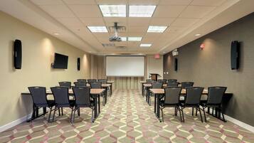 A conference room with a projector, screen, and multiple tables with chairs.