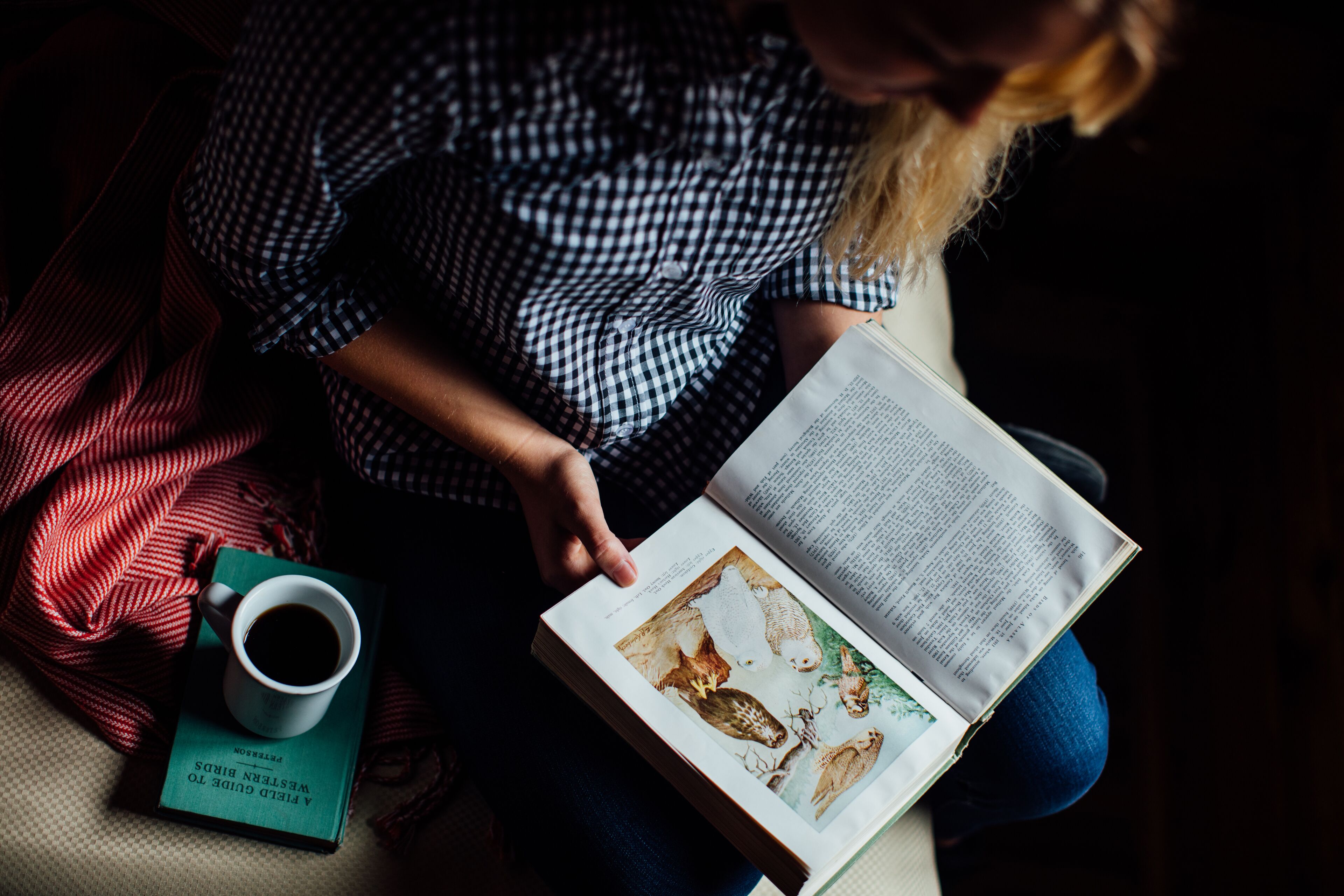 A person reading a book with a cup of coffee beside them.