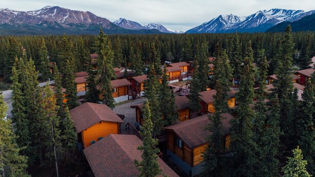 A lodge with multiple wooden cabins surrounded by dense forest and mountains in the background.