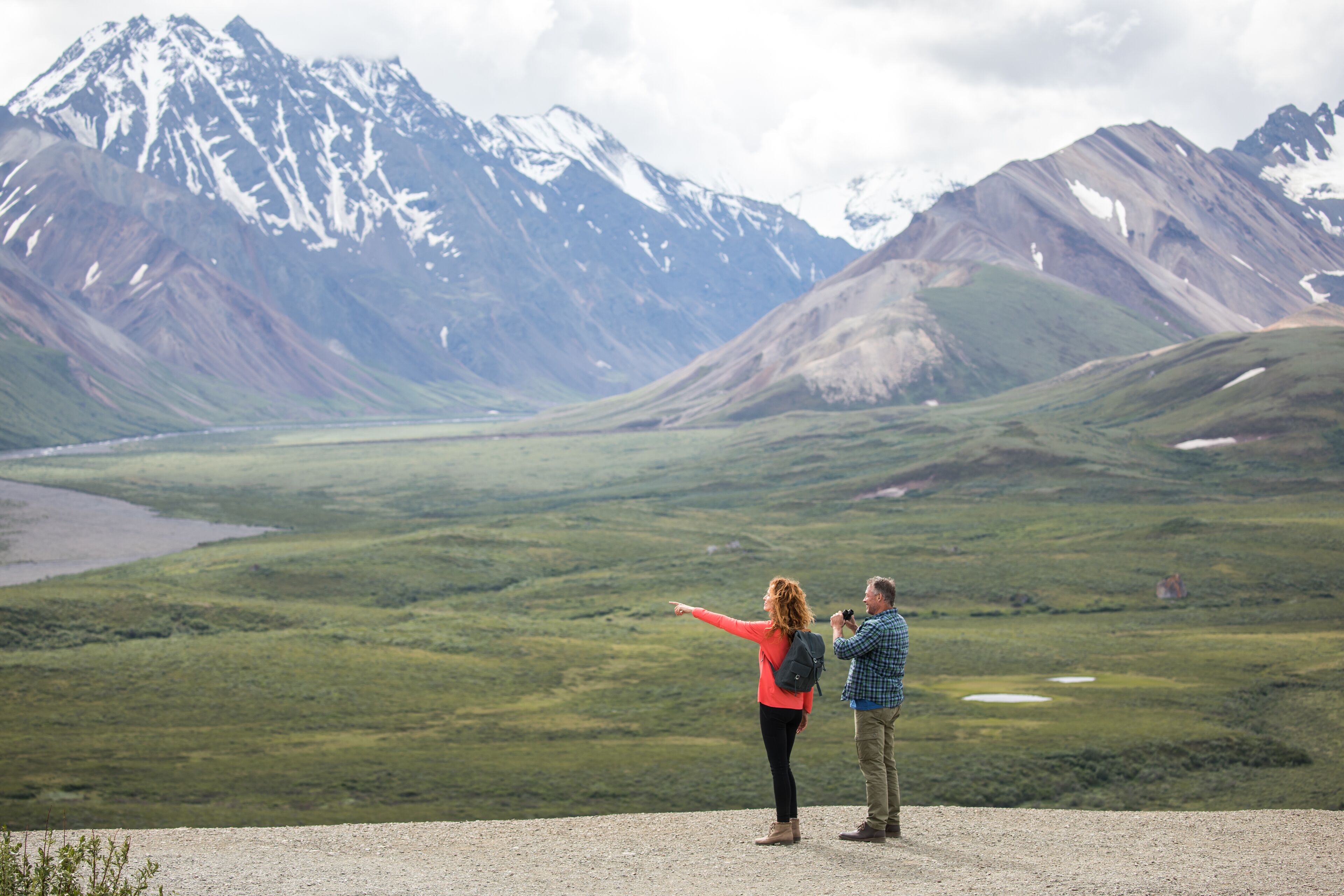 A couple standing on a gravel path with a mountainous landscape in the background.