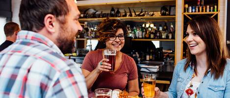 Un grupo de personas sentadas en una mesa de madera en un bar, con estantes llenos de botellas y vasos al fondo.